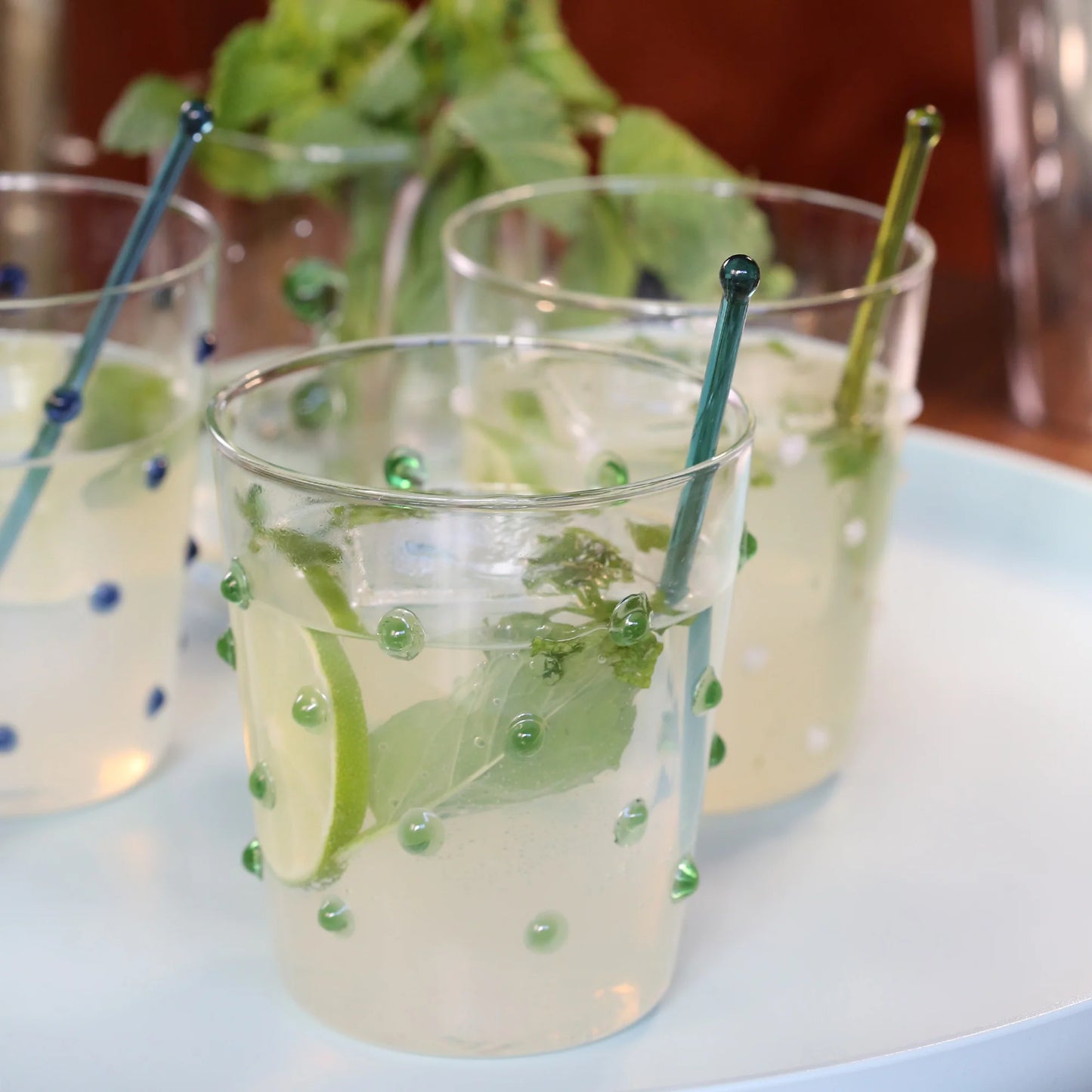 Three glasses of lemonade with lime slices and mint leaves on a white surface.