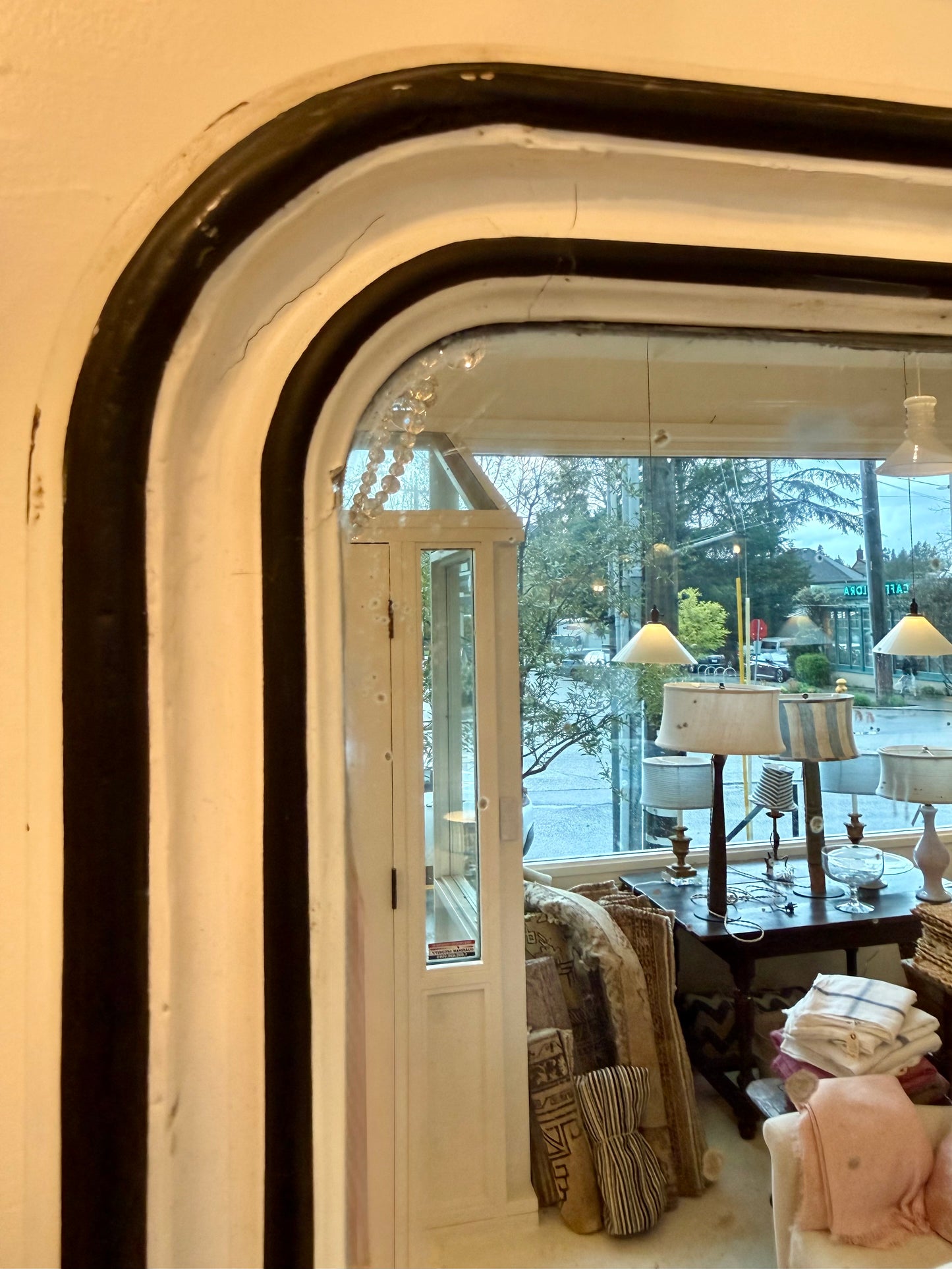 View from inside the store through a large arched vintage mirror, showing various furniture and decor.