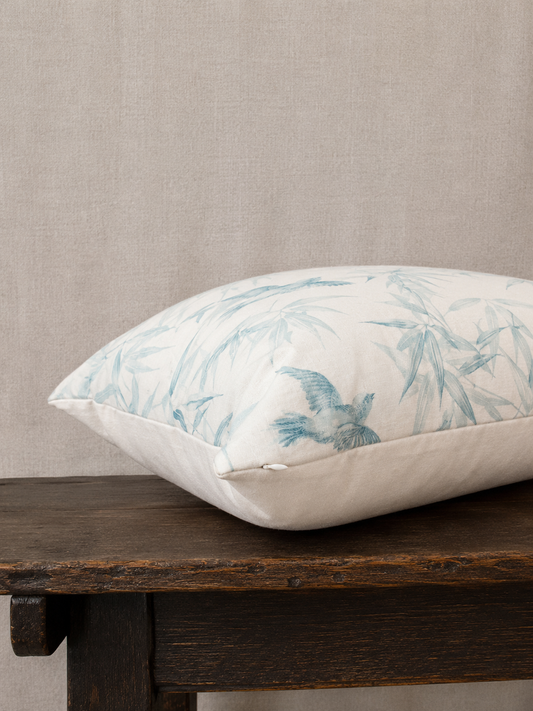 Decorative pillow with bird and leaf pattern on a wooden bench against a beige wall