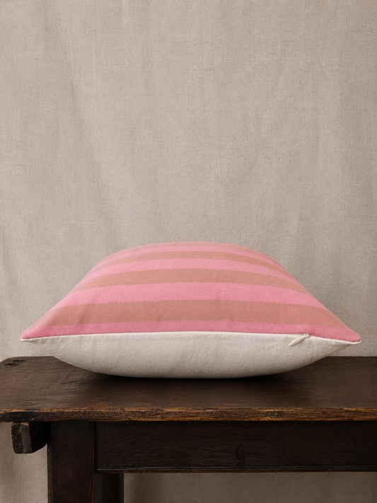 Striped pink and beige pillow on a wooden bench against a beige wall