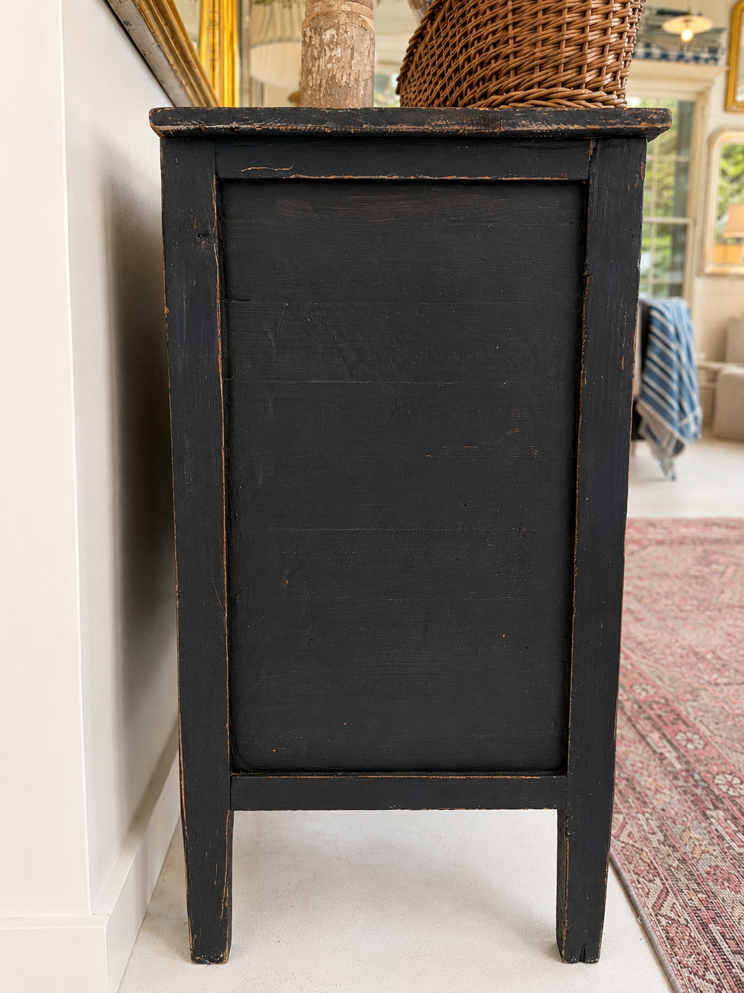 Side view of a black wooden table in a room with a mirror and rug.