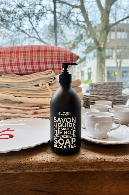Black soap bottle labeled 'Savon Liquide de Marseille' on a wooden surface with a blurred background.