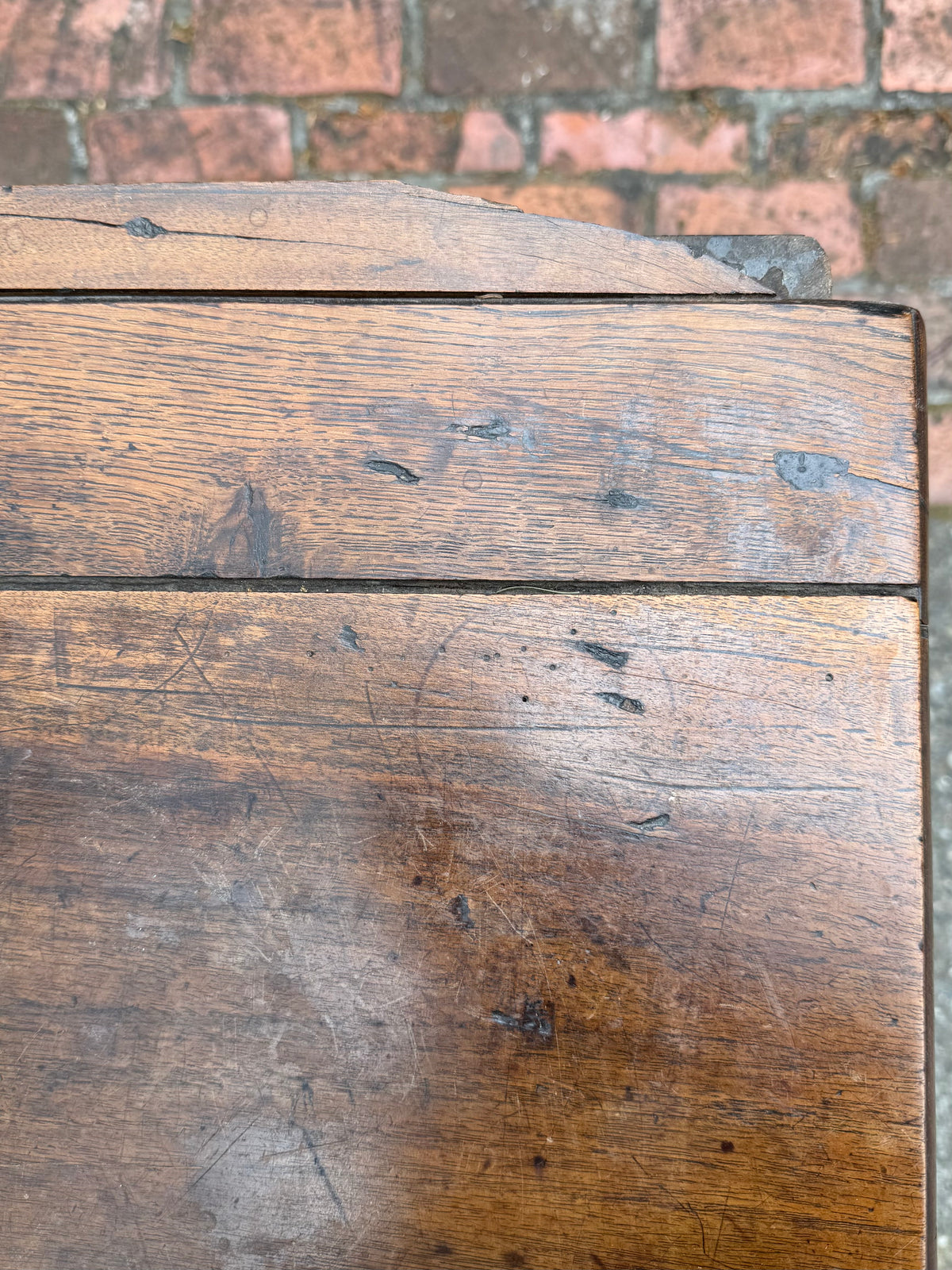 Close-up of a wooden surface with visible grain and wear, set against a brick wall background.