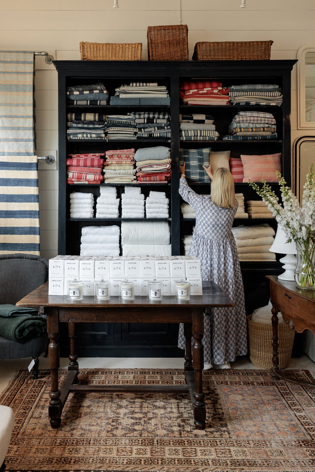 Founder organizing folded fabrics in a large black cabinet with a table in front displaying boxes.