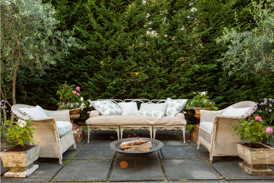 Outdoor patio with wicker furniture, fire pit, and greenery