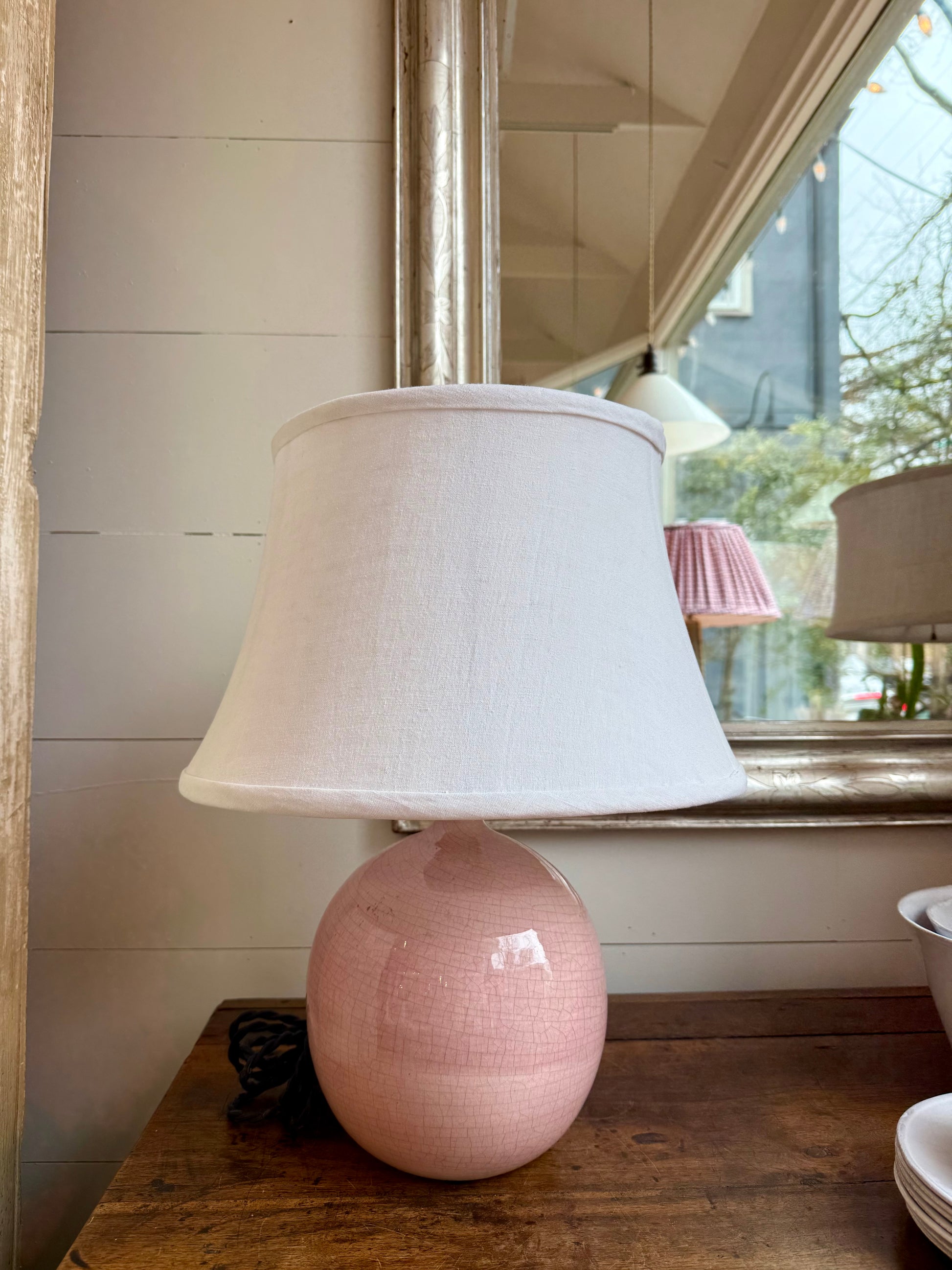 Pink ceramic lamp with a white lampshade on a wooden surface.
