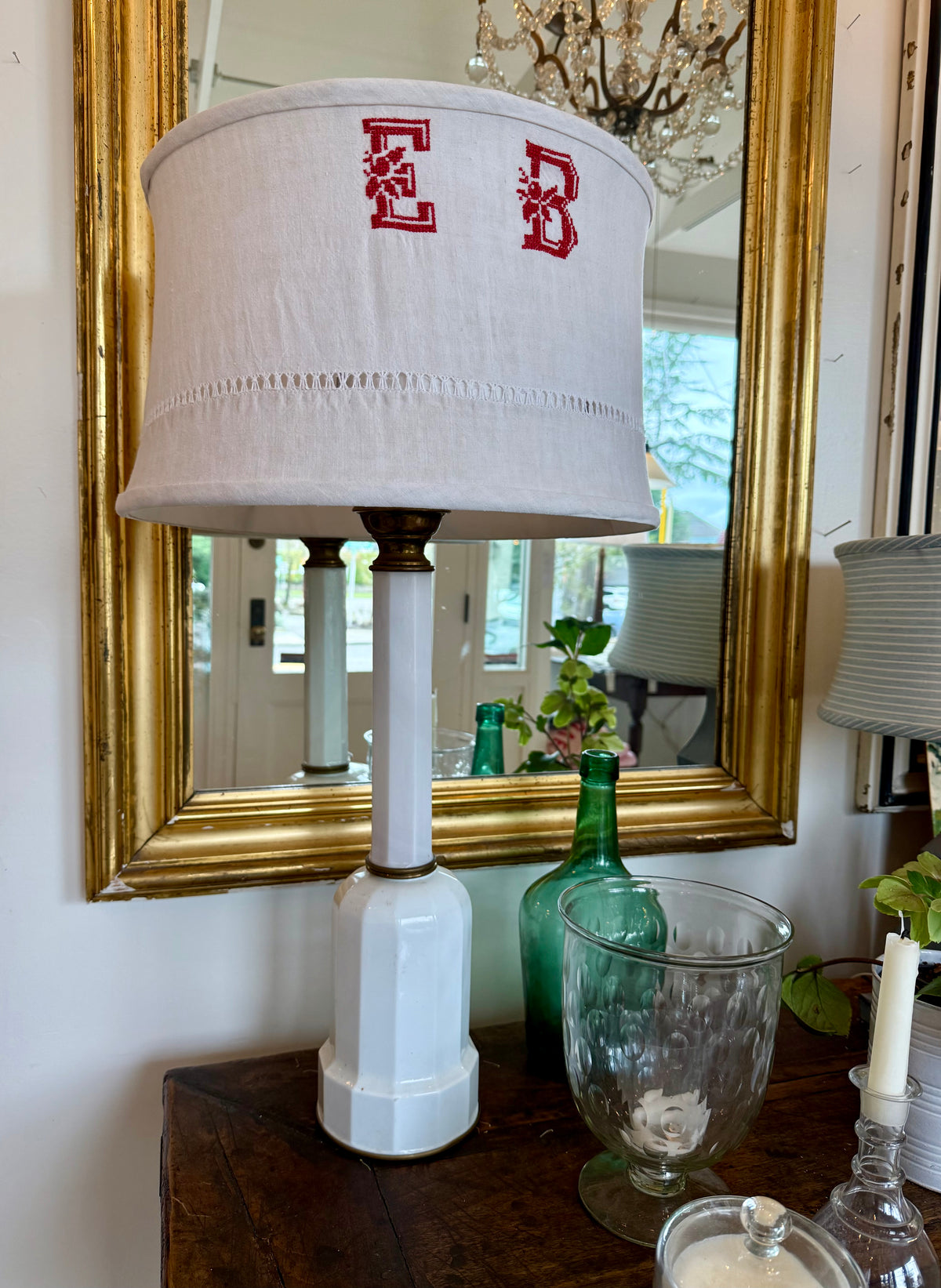 Lamp with monogrammed shade in front of a mirror on a table.