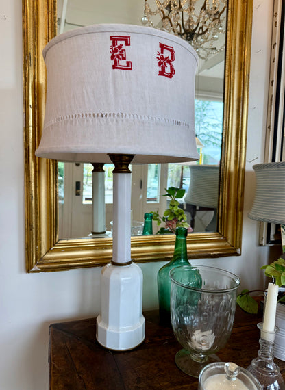 Lamp with monogrammed shade in front of a mirror on a table.