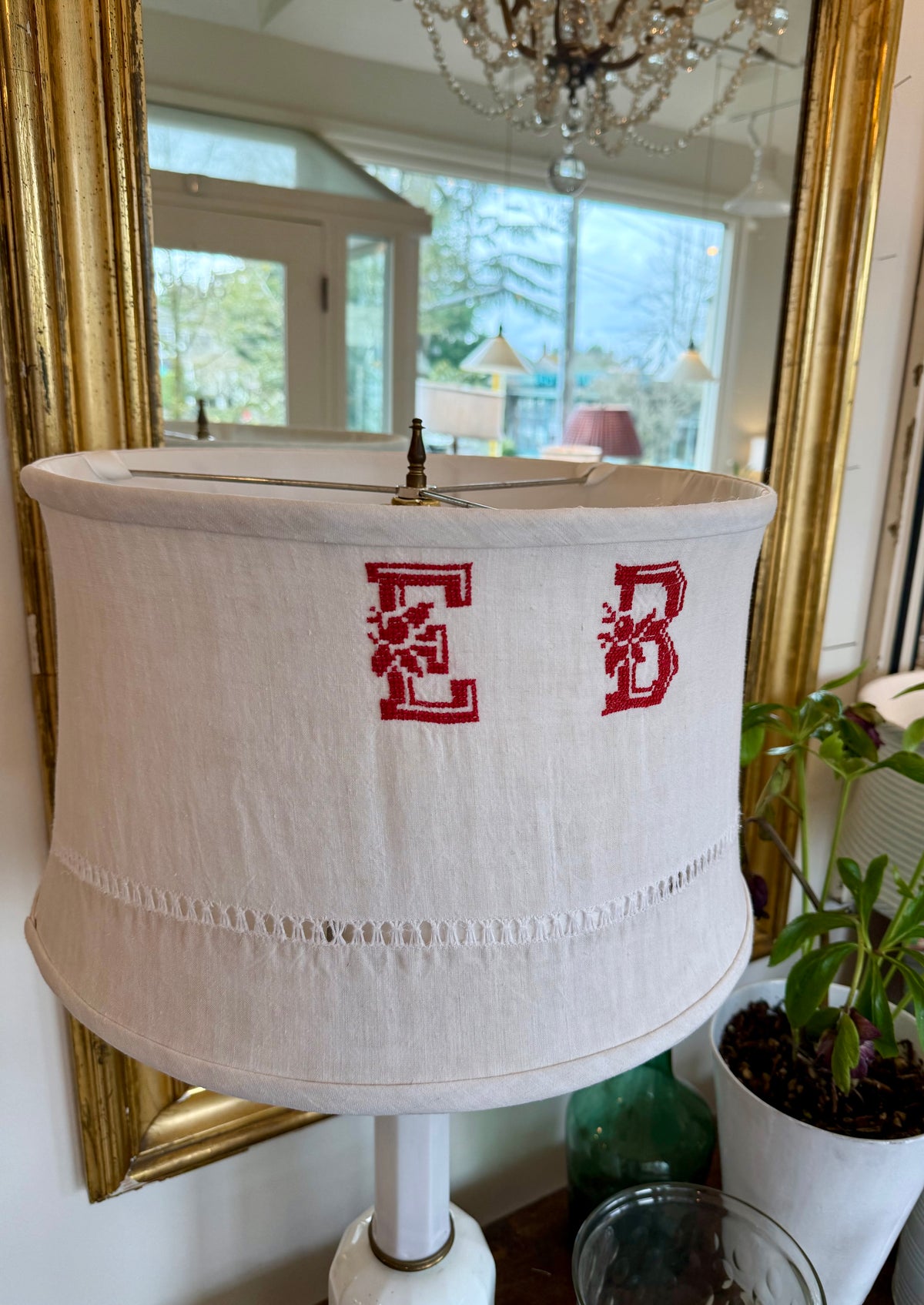 White lampshade with red initials 'EB' in a room with a mirror and plant.