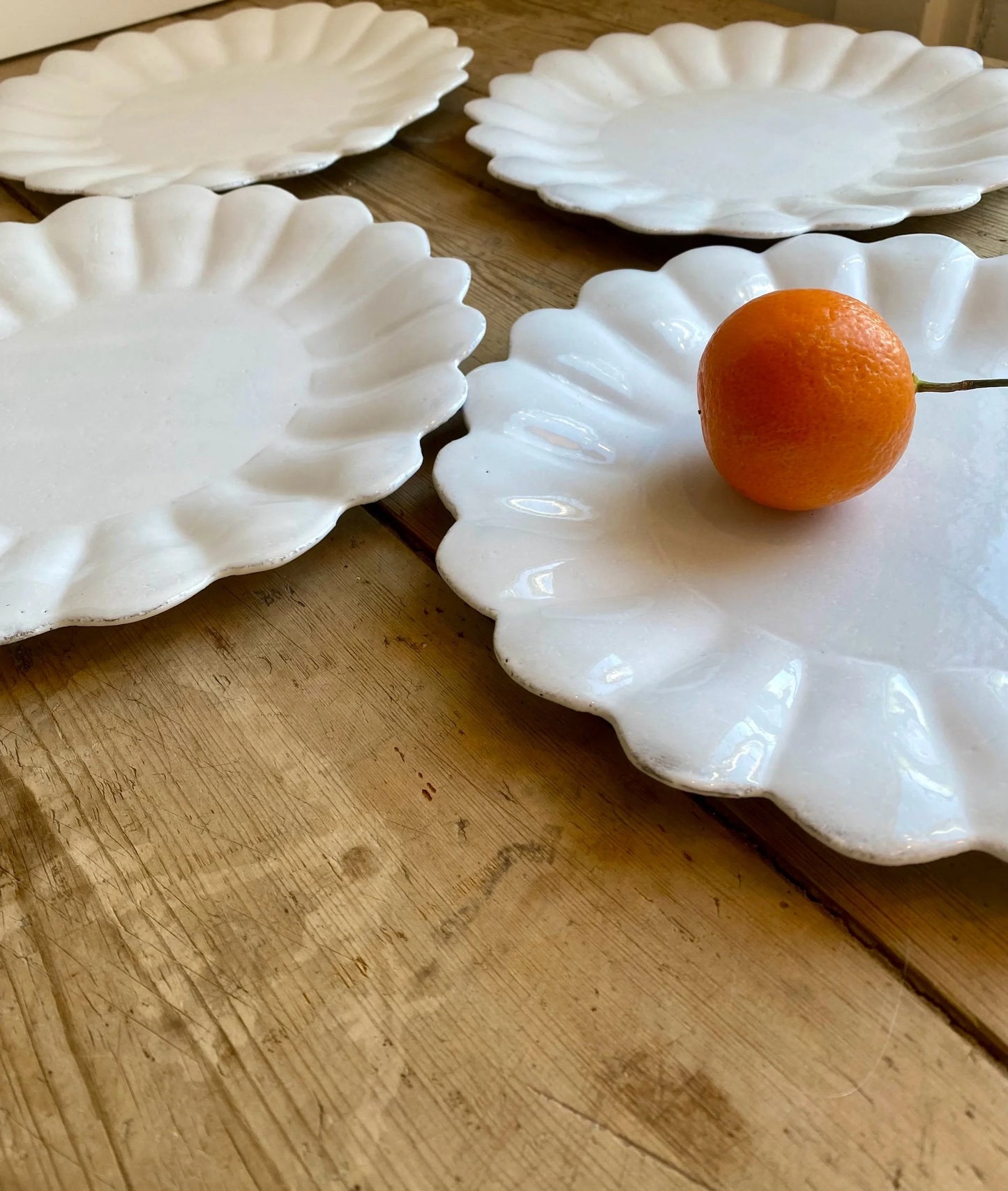 White scalloped-edge plates on a wooden surface with an orange fruit on one plate.