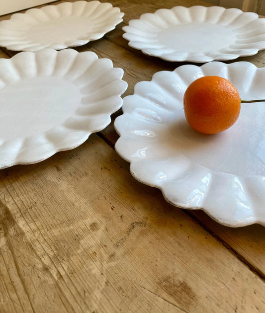 White scalloped-edge plates on a wooden surface with an orange fruit on one plate.