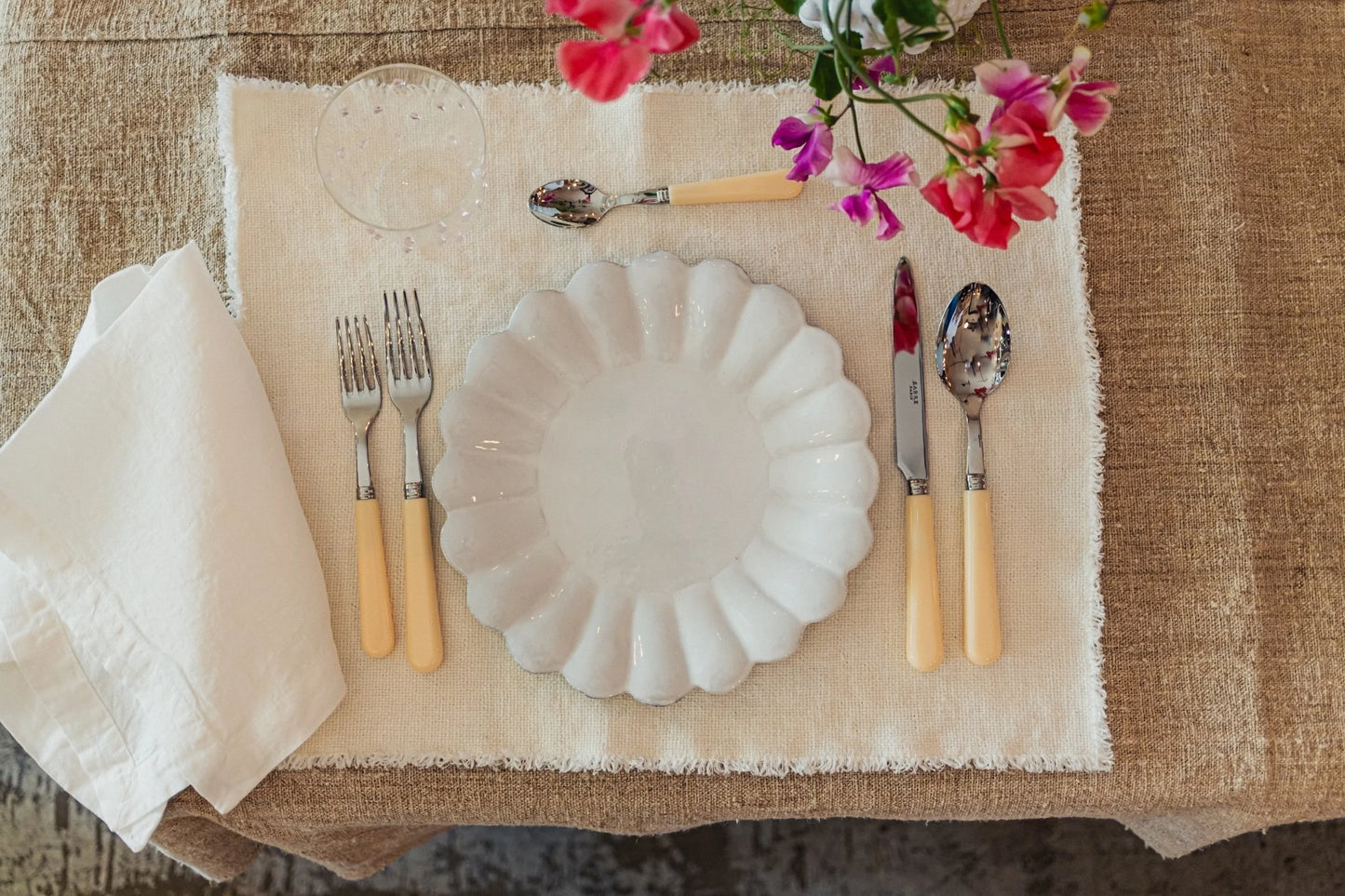 Table setting with white plate, cutlery, and pink flowers on a textured surface
