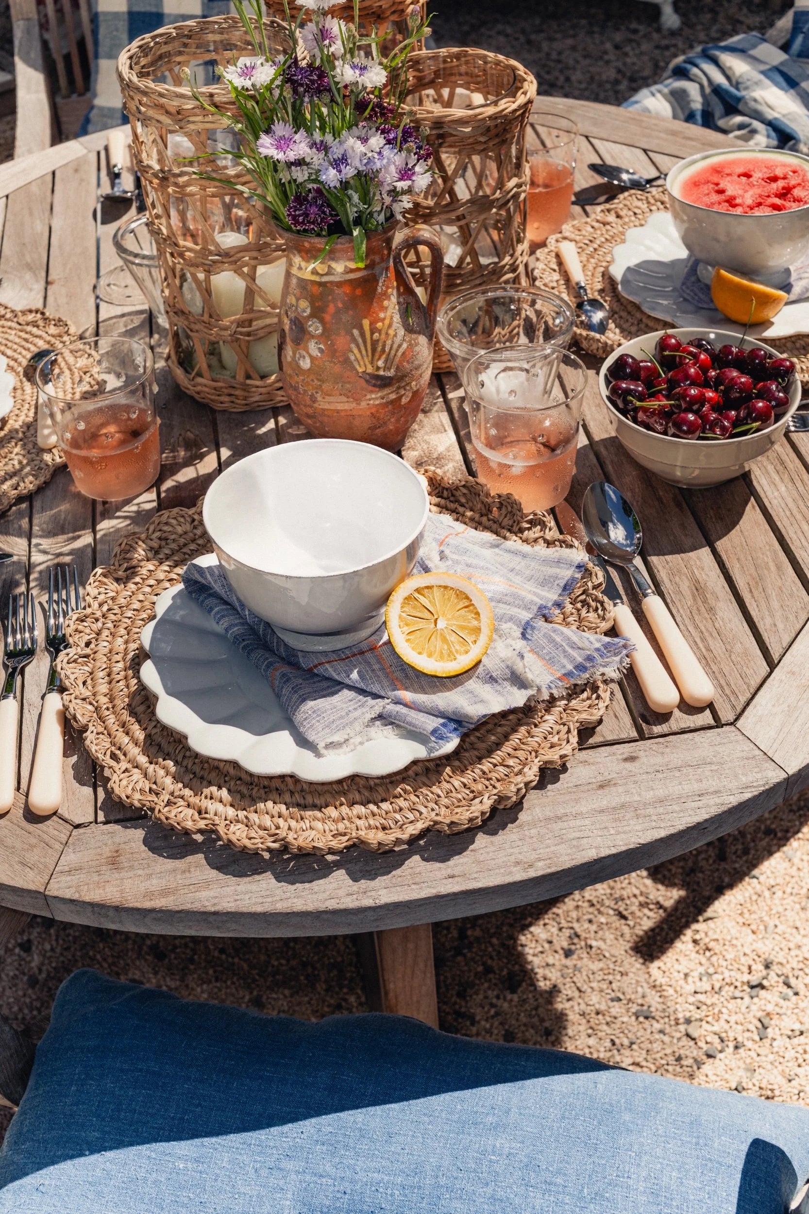 Outdoor dining table set with bowls, cutlery, and drinks on a wooden table.