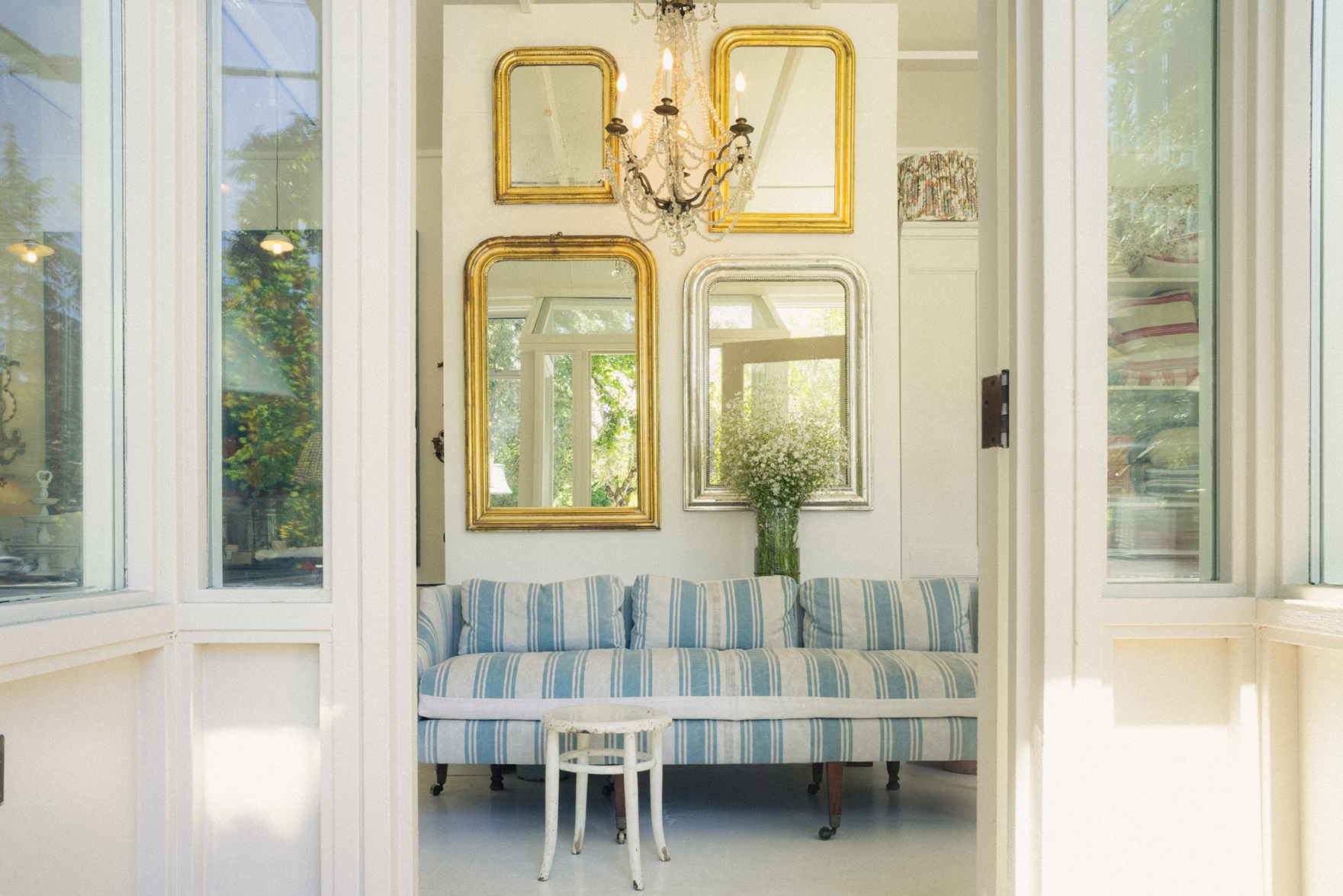 Living room look view in red ticking store with striped sofa, gold-framed mirrors, and a chandelier.
