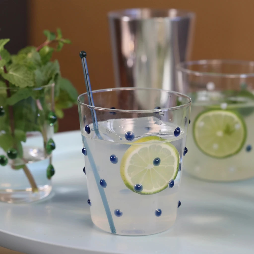 Clear glass with blue dots with lemon and lime slices, blueberries, and a straw on a white surface.
