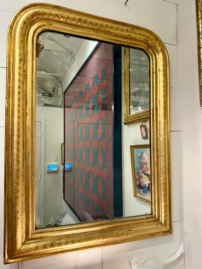 Gold-framed mirror on a tiled wall with reflections of a room.