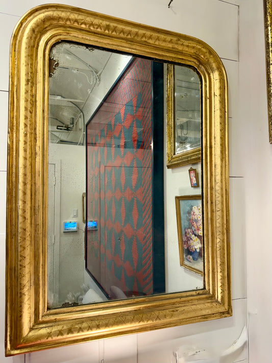 Gold-framed mirror on a tiled wall with reflections of a room.