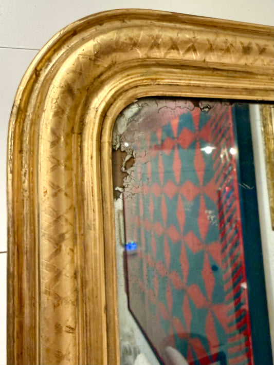 Gold-framed mirror with reflective surface showing colorful fabric pattern