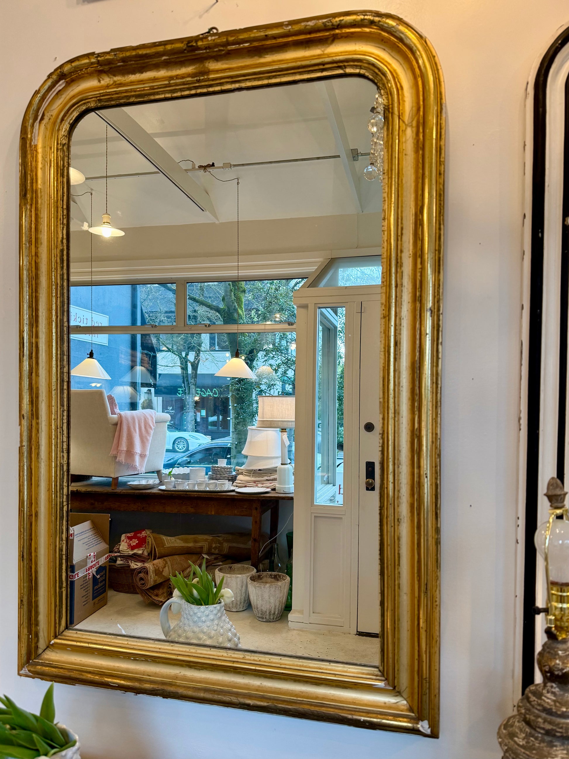 Large ornate gold-framed mirror on a wall with a reflection of the store interior.