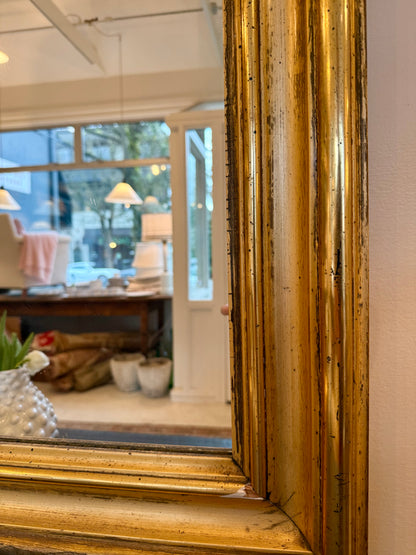 Gold-framed mirror reflecting the store with furniture and decor.