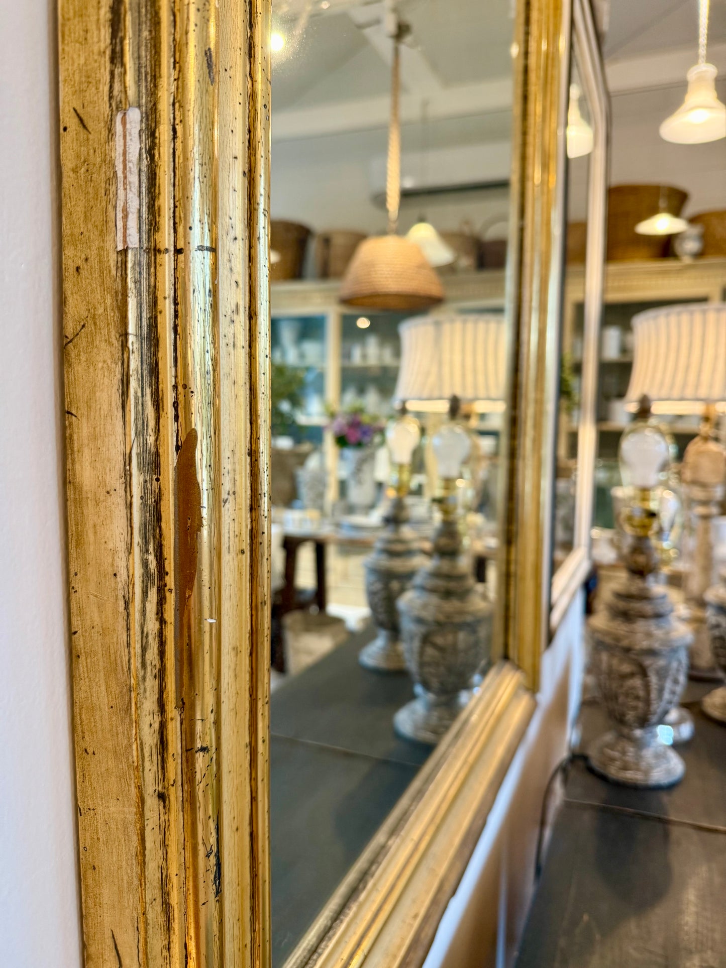 Gold-framed mirror reflecting a store interior with lamps and decor.