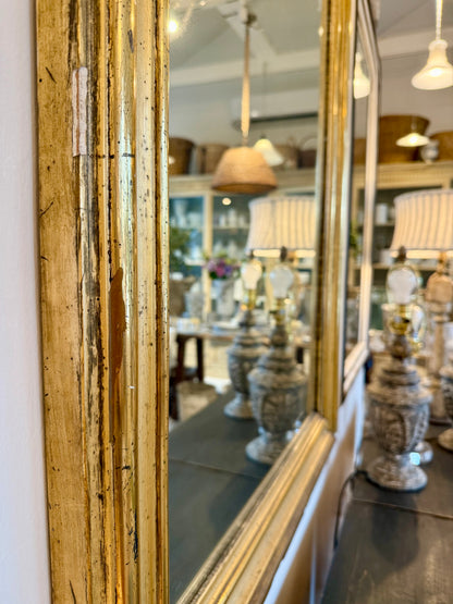 Gold-framed mirror reflecting a store interior with lamps and decor.