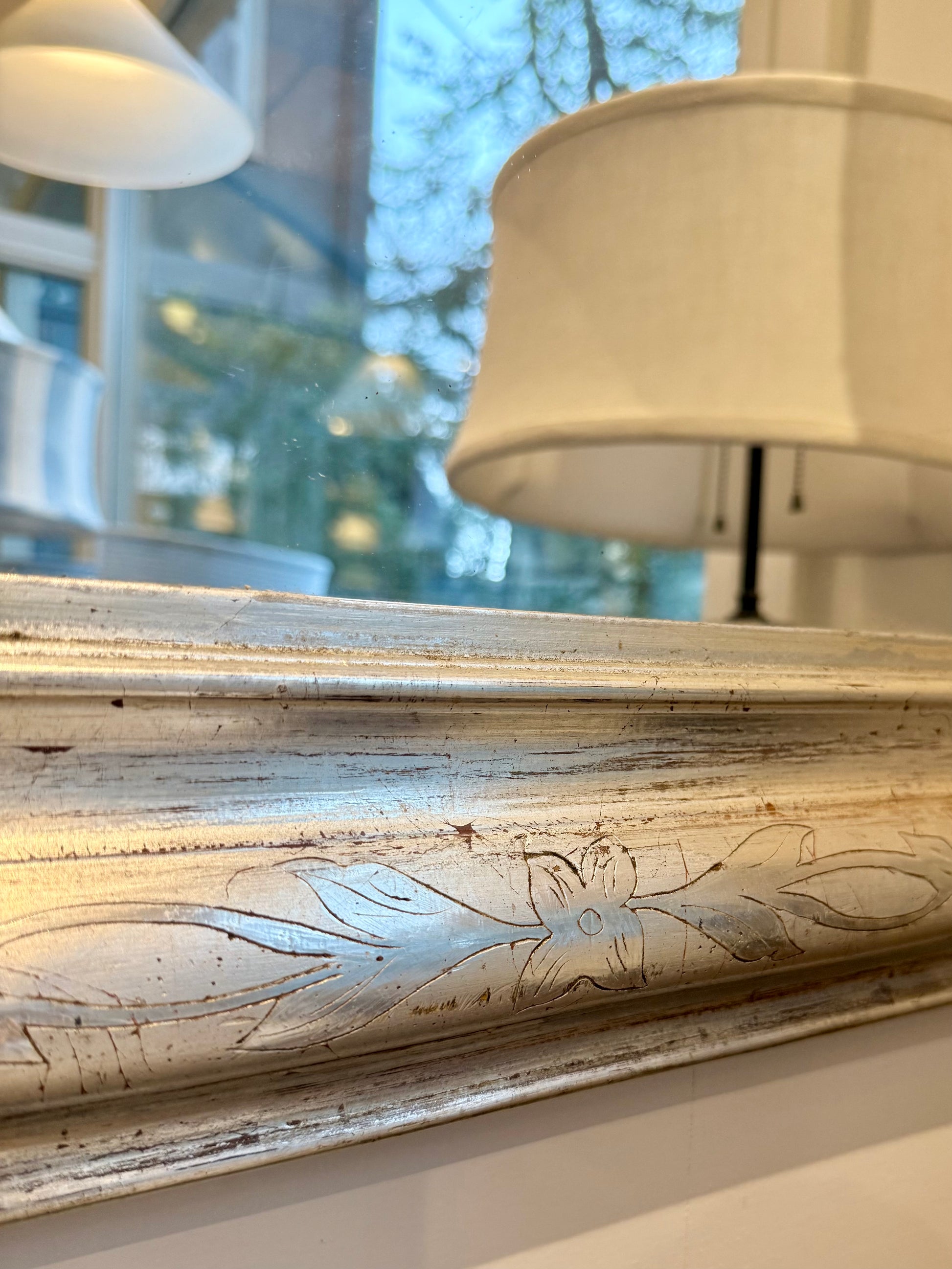 Decorative vintage mirror with engraved design and hanging at the bottom with reflection of lampshades. and outdoor scene. 
