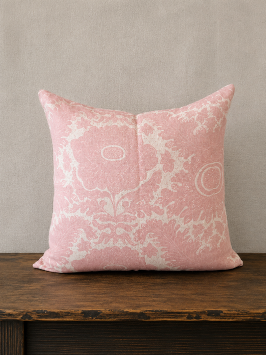 Pink decorative pillow with white patterns on a wooden surface and beige wall background