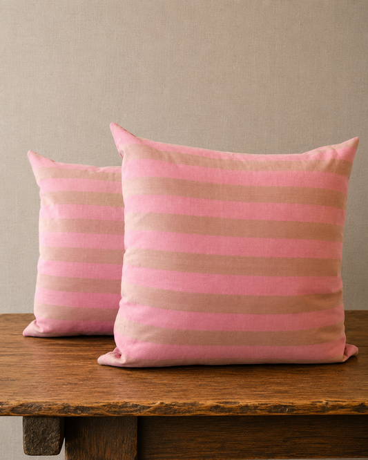 Two pink and brown striped pillows on a wooden surface with a neutral background