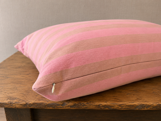 Pink striped pillow on a wooden surface with a neutral background