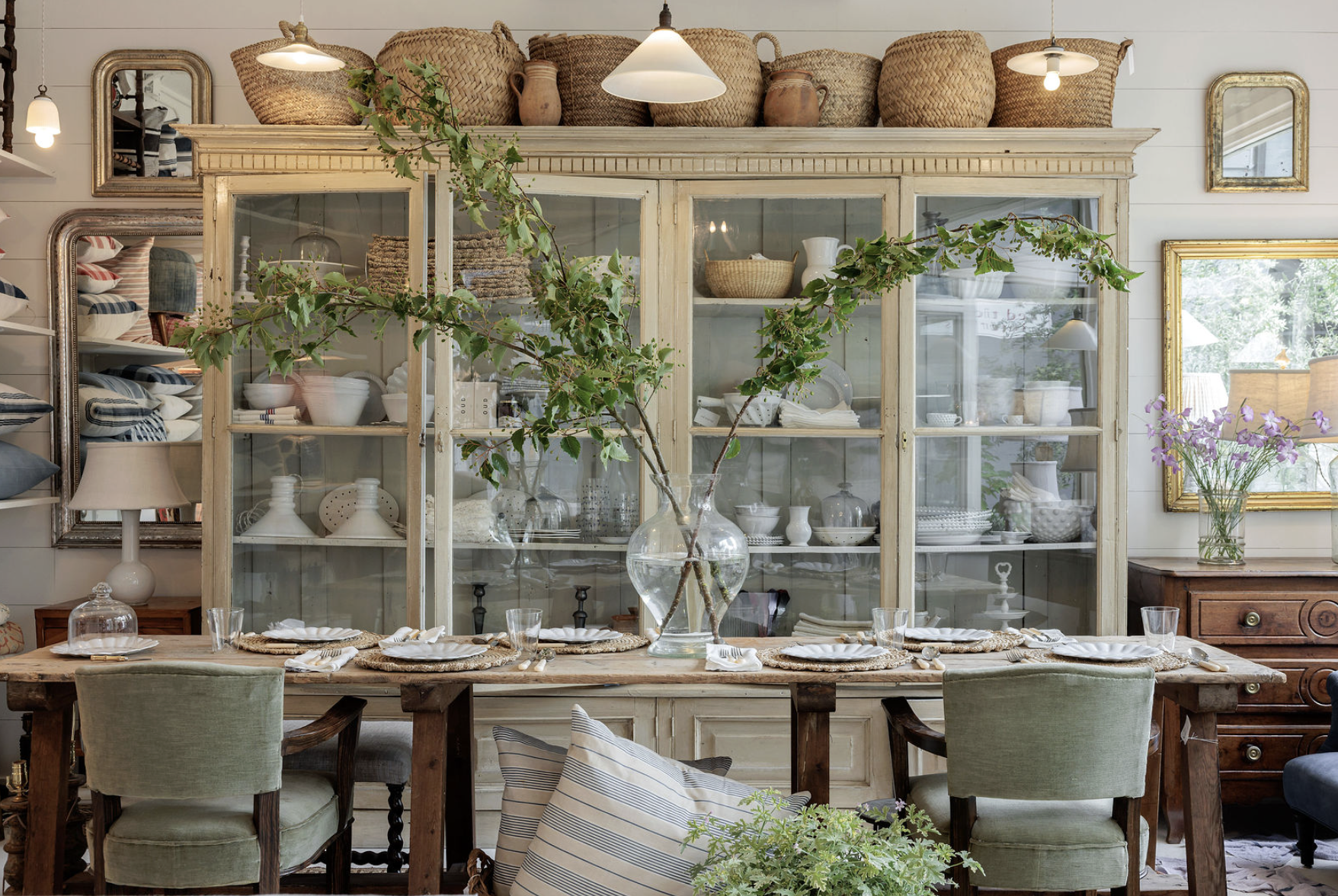Red Ticking Shop with a large white china cabinet, wooden table, chairs and decor styled throughout. 
