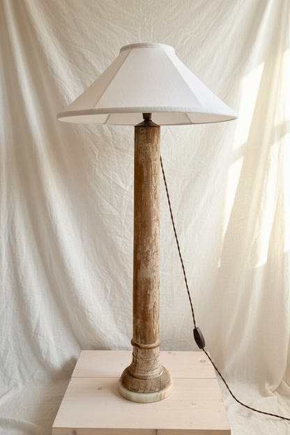 Tall vintage lamp with a white shade on a wooden base against a white curtain background