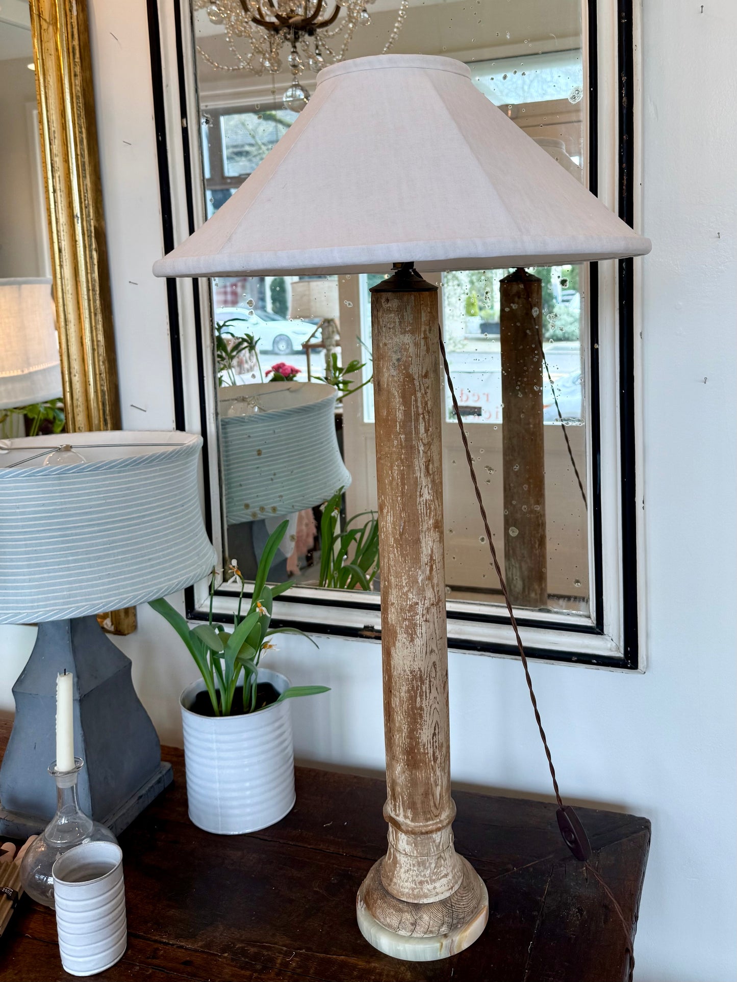 Table lamp with wooden base and white shade on a table in front of a mirror.