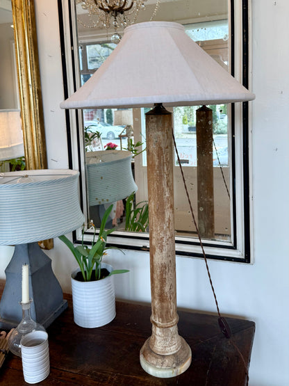 Table lamp with wooden base and white shade on a table in front of a mirror.