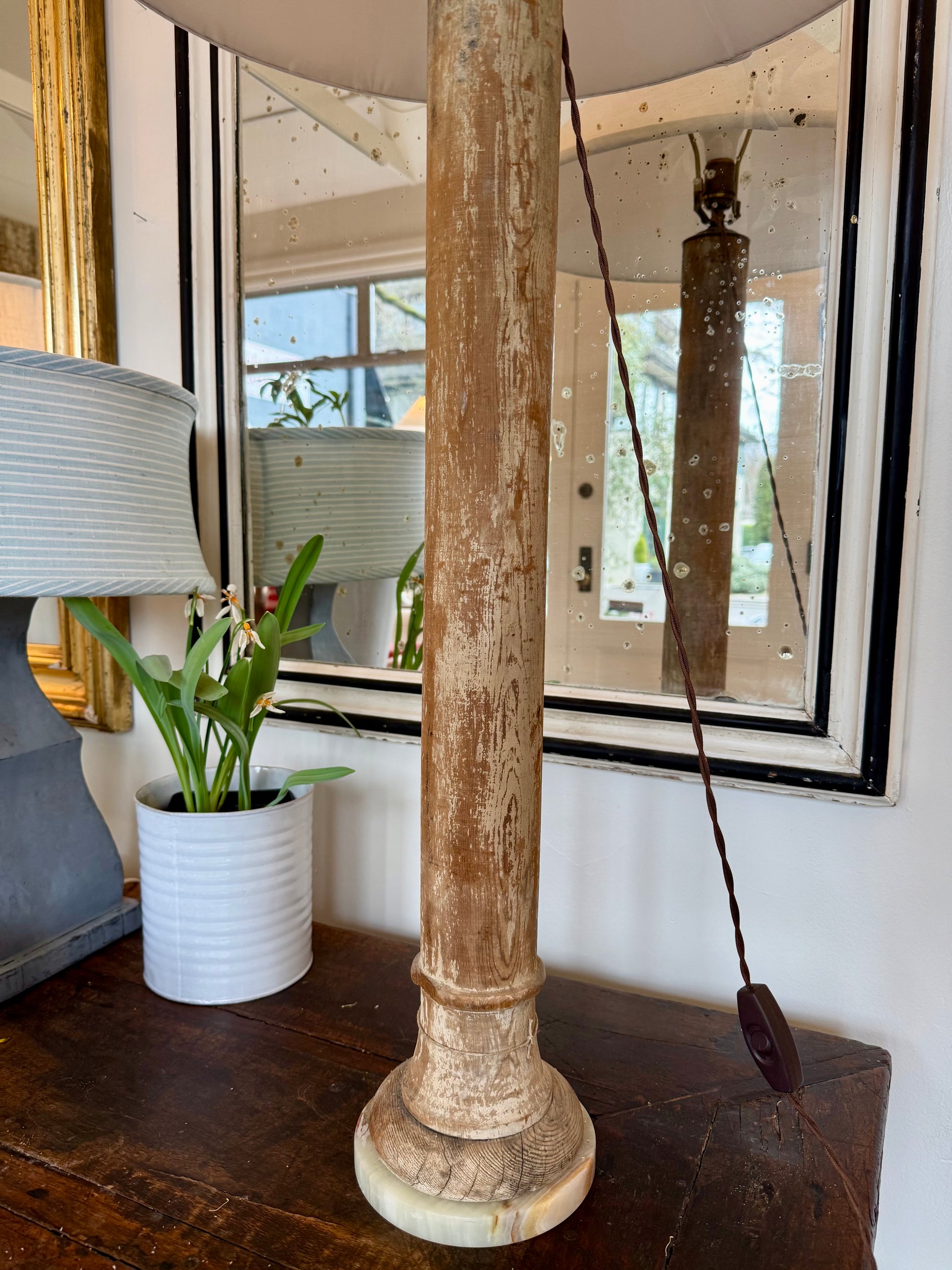 Decorative lamp with wooden base and white shade in the store with a mirror and plant next to it. 