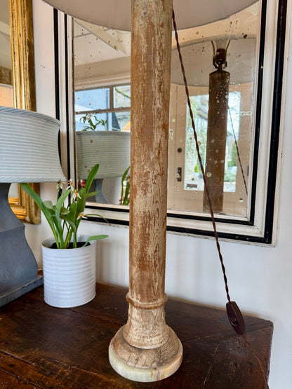 Decorative lamp with wooden base and white shade in the store with a mirror and plant next to it. 