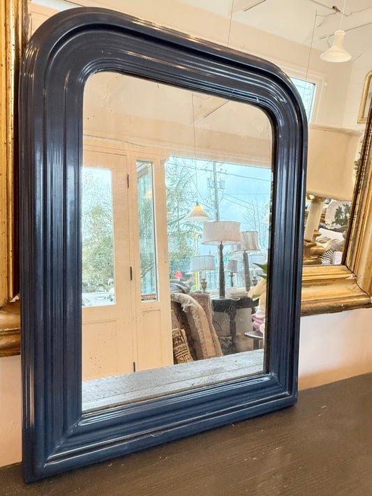 Navy blue framed mirror on a wooden floor with a blurred indoor background