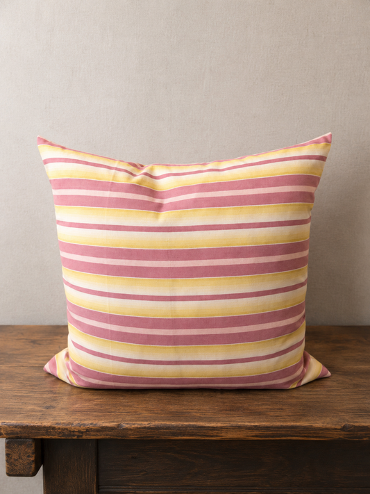Striped pillow with pink and yellow pattern on a wooden surface against a beige wall