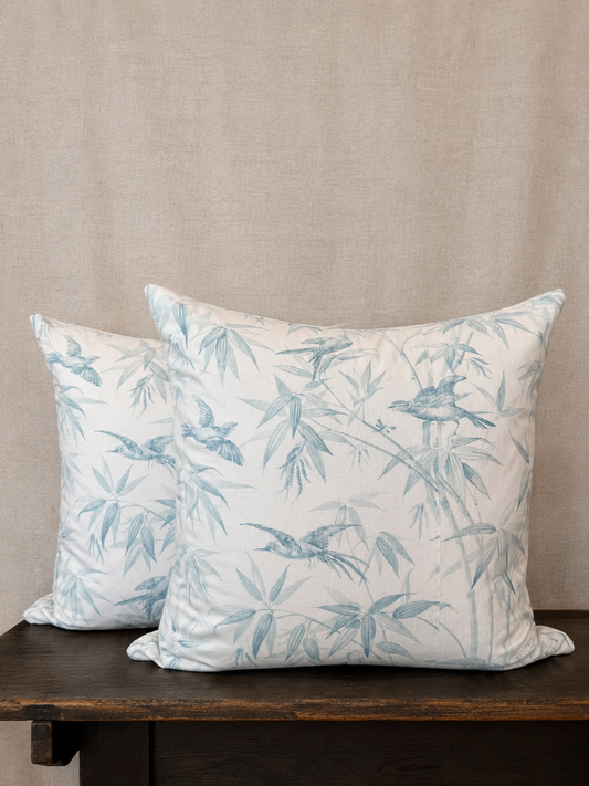 Two decorative pillows with blue bird and leaf pattern on a wooden surface against a beige wall.