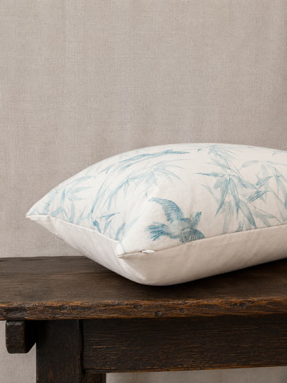 Decorative pillow with bird and leaf pattern on a wooden bench against a beige wall