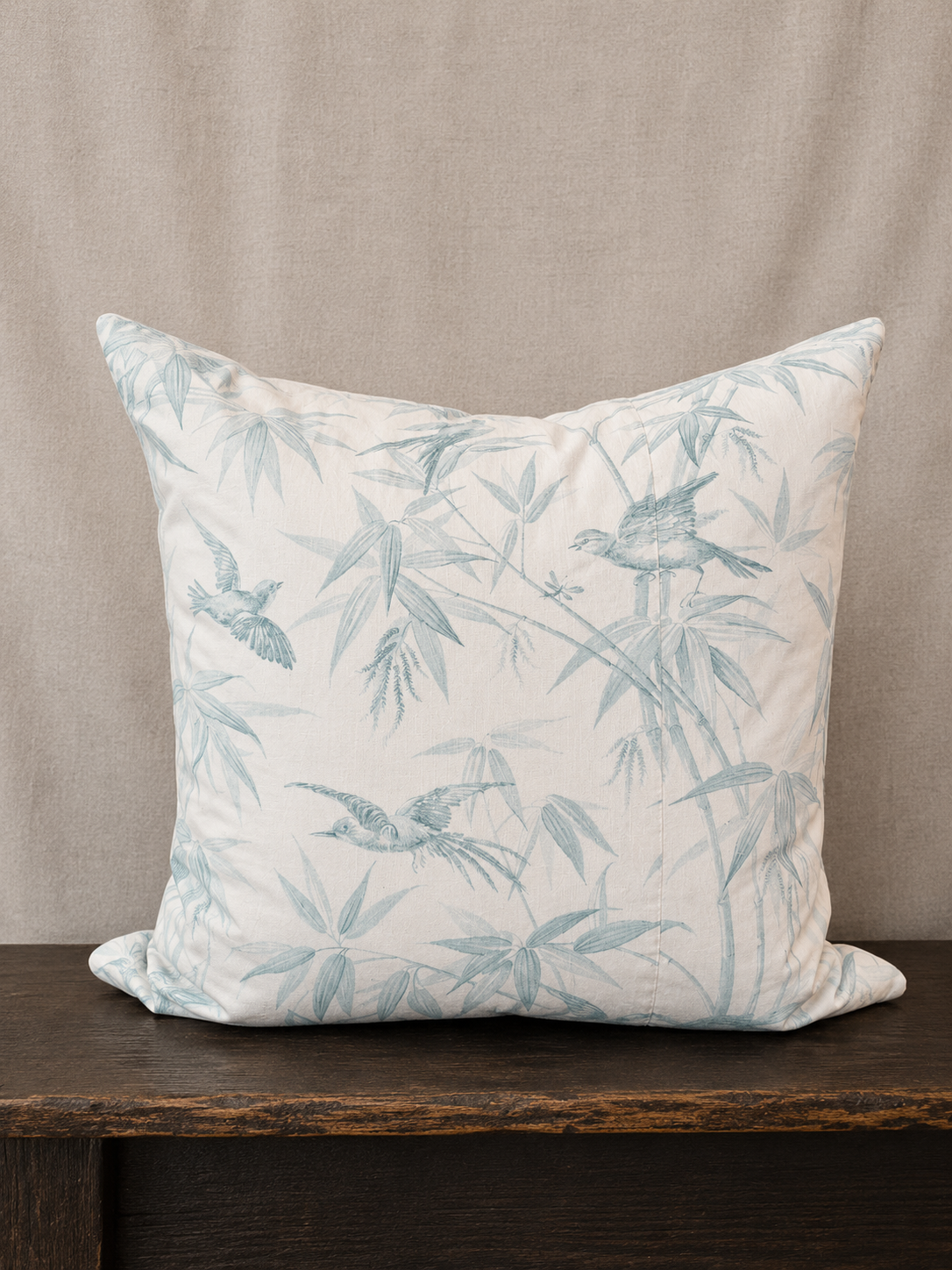 Decorative pillow with bird and leaf pattern on a wooden surface and beige background