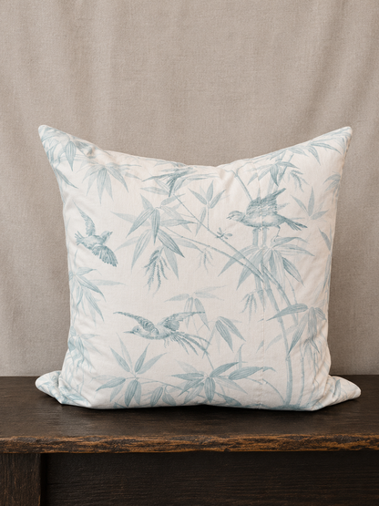 Decorative pillow with bird and leaf pattern on a wooden surface and beige background