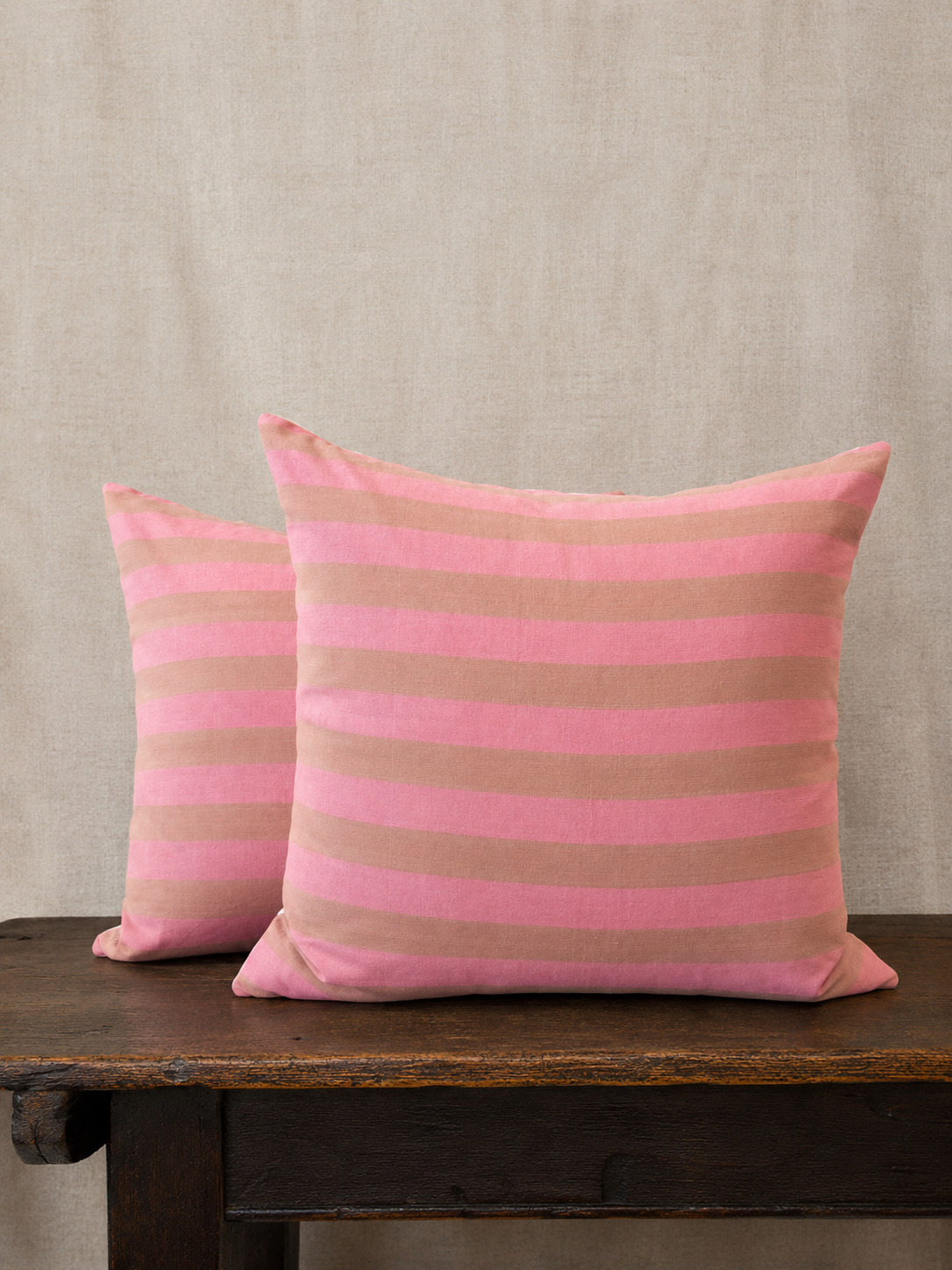 Two pink and beige striped pillows on a wooden surface with a beige background