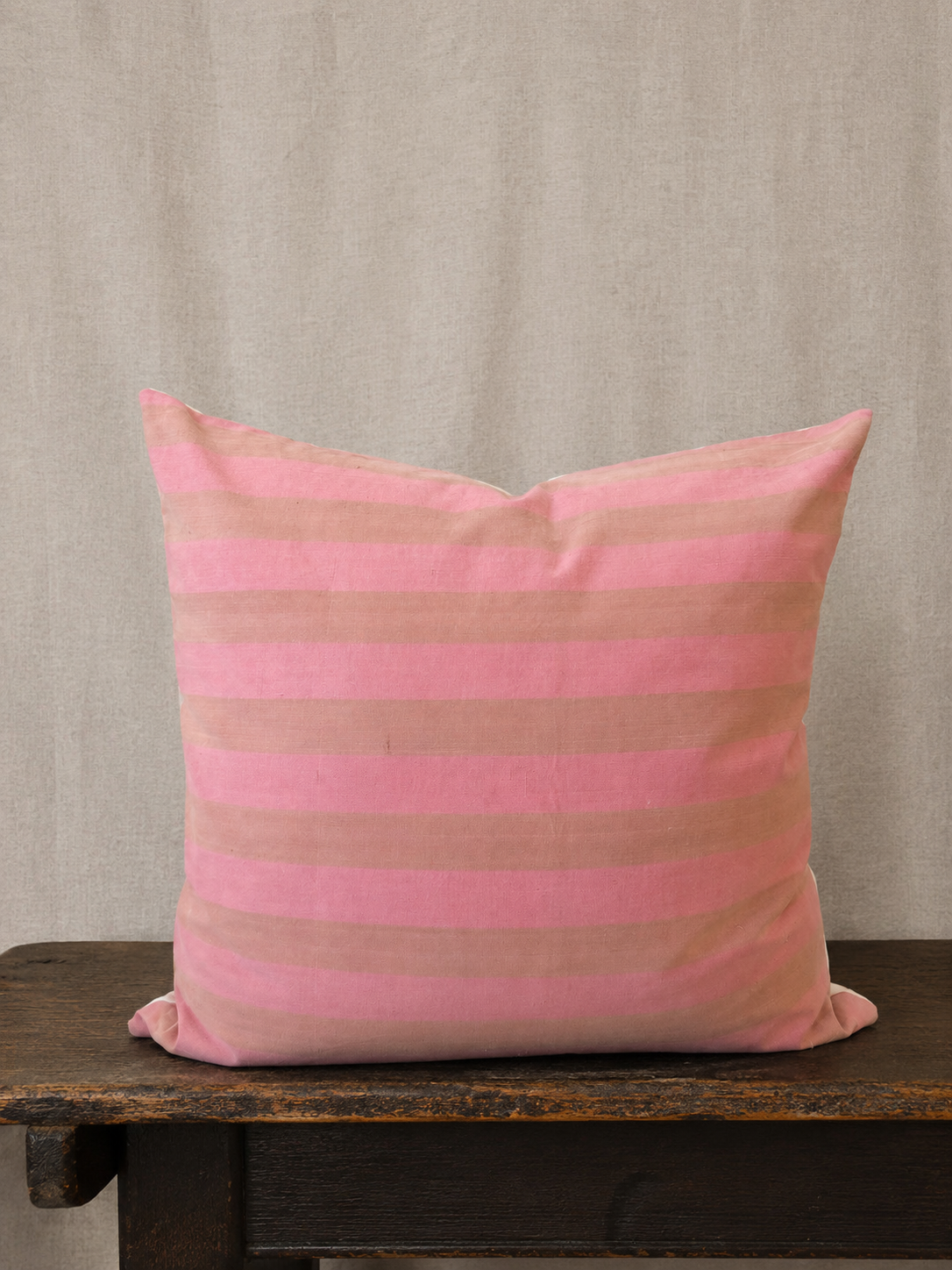 Pink and beige striped pillow on a wooden surface with a beige background