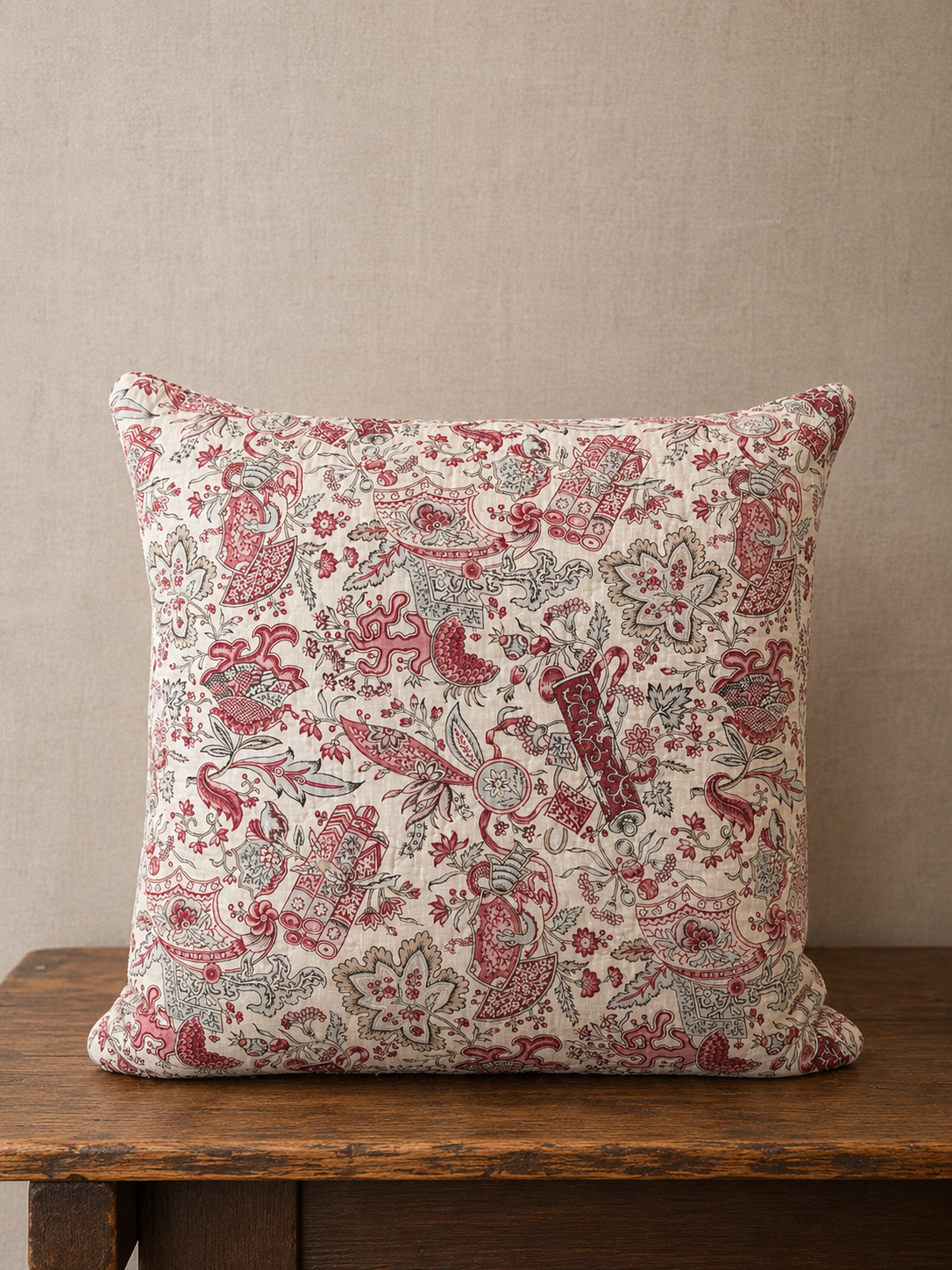 Decorative pillow with red and beige pattern on a wooden surface against a beige wall