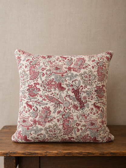 Decorative pillow with red and beige pattern on a wooden surface against a beige wall