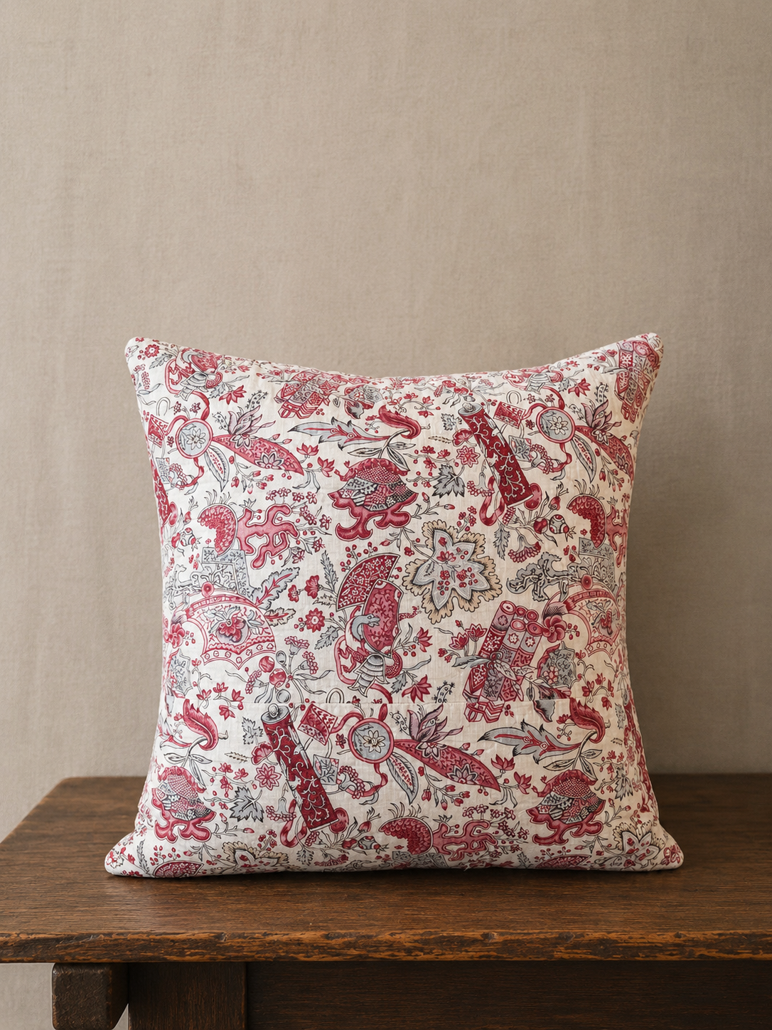 Decorative pillow with a red floral pattern on a wooden surface against a beige wall