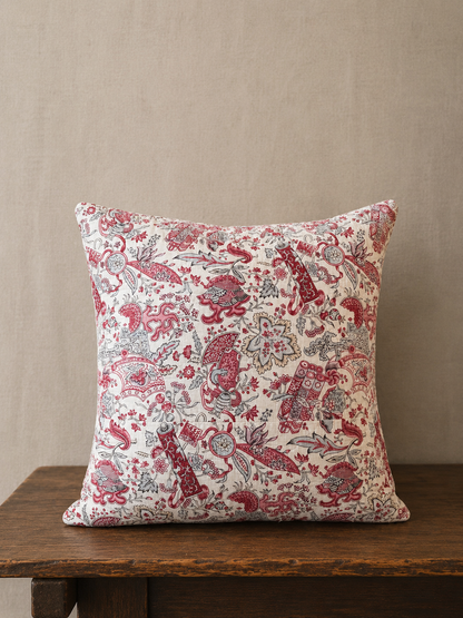 Decorative pillow with a red floral pattern on a wooden surface against a beige wall