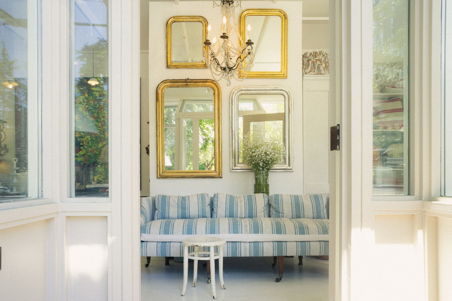 Red Ticking Shop entrance with striped sofa, gold-framed mirrors on white wall, and a chandelier when you walk in. 