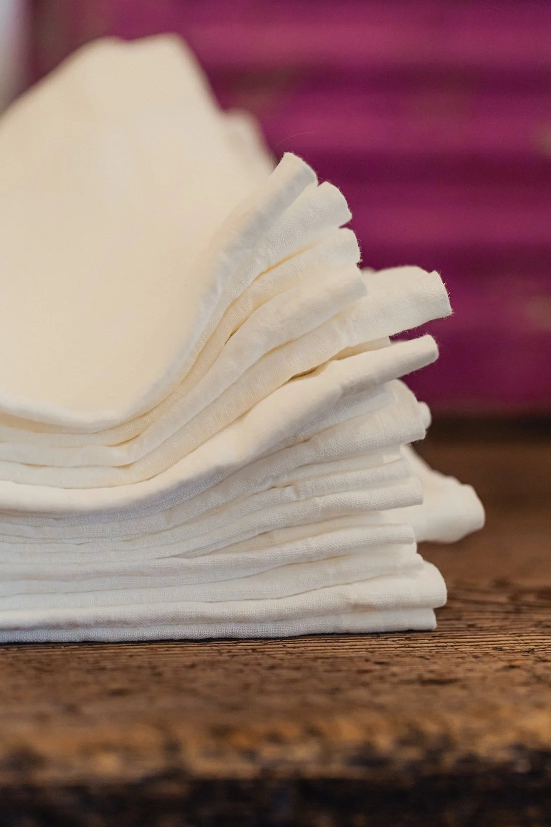 Stack of white napkins on a wooden surface with a blurred purple background